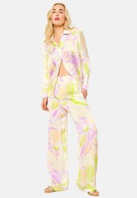Langermige blouse met bloemenpatroon en wijde broek in pastelroze, paars en groen op een lichte achtergrond. Zacht, glad materiaal.