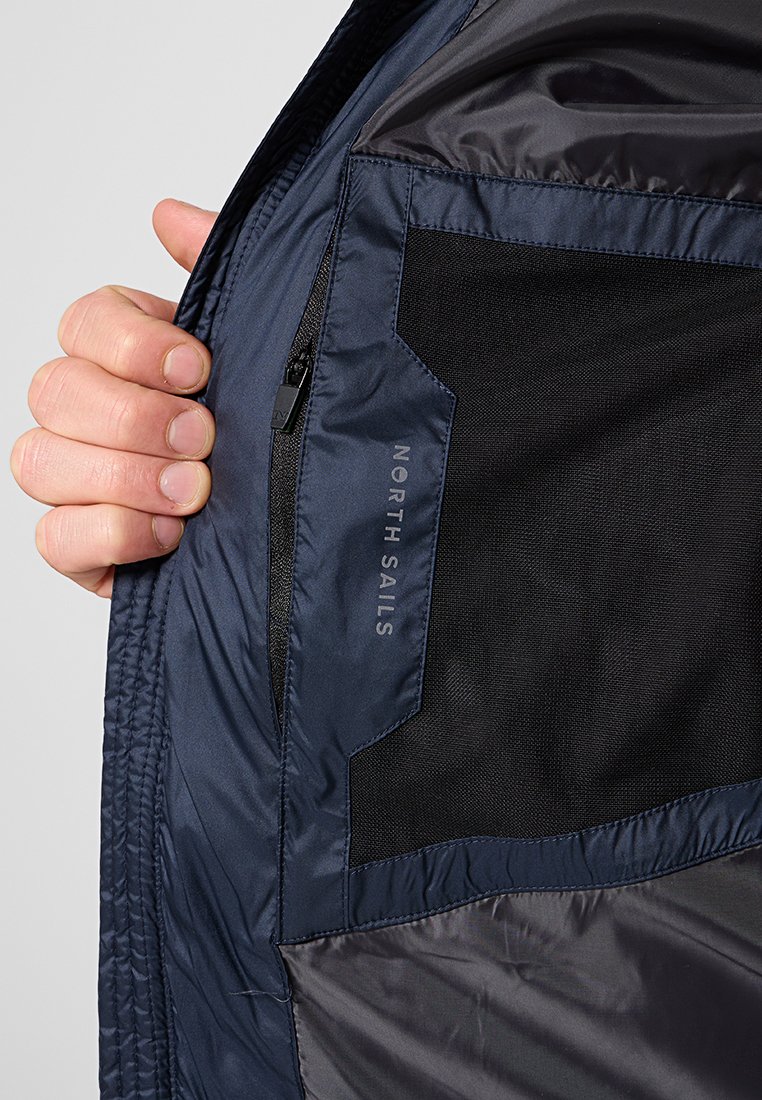Granatowa lekka kurtka z zamkiem błyskawicznym i siateczkową podszewką. Charakteryzuje się gładką fakturą oraz logo "NORTH SAILS" w kontrastowym kolorze.