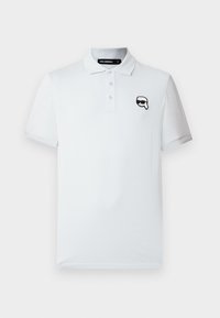 Polo blanc à manches courtes avec trois boutons et un petit logo noir et blanc représentant un visage portant des lunettes de soleil sur la poitrine gauche.