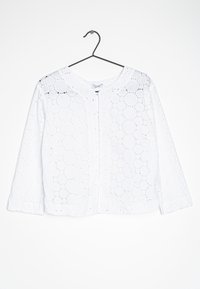 Vit blus i broderad bomull, med cirkulära utskärningar, rund halsringning och lång ärm. Knäppt framtill.