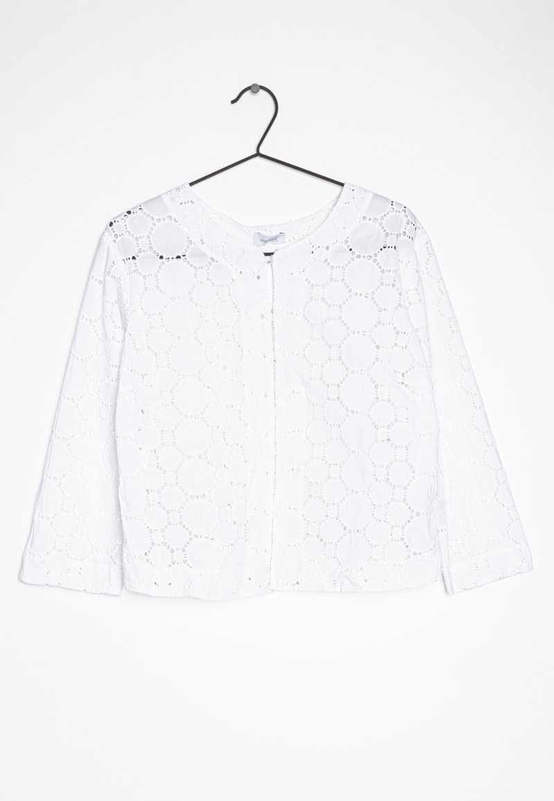 Vit blus i broderad bomull, med cirkulära utskärningar, rund halsringning och lång ärm. Knäppt framtill.