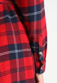 Tessuto flanella a quadri rossi e blu navy con dettagli ai polsini a bottoni. Presenta grandi quadrati alternati a sottili righe bianche. Texture morbida.