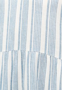 Υφασμα με κάθετες μπλε και λευκές ρίγες και ραφή που συγκεντρώνει το ύφασμα, δημιουργώντας ελαφριές πιέτες κατά μήκος της οριζόντιας γραμμής ραψίματος.