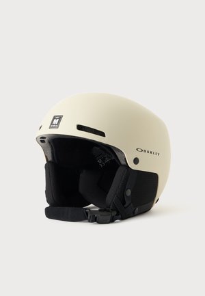 Cremefarvet Oakley skihjelm med sorte polstrede ørekopper og justerbar hagebøjle, størrelse medium 55-58 cm.