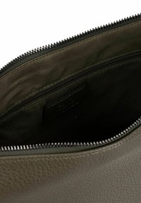 Interior de bolsa de cuero verde oliva con cierre de cremallera, exterior texturizado, forro de tela suave y un pequeño bolsillo interno visible.