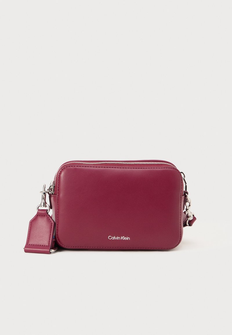 Bordo kožni crossbody predmet sa srebrnim hardverom, zatvaranjem na patentni zatvarač i utisnutim logotipom. pravokutni oblik s odvojivim remenom.
