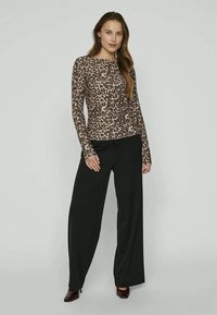 Pikkade varrukatega leopardimustriga topp, pruunide ja beežide toonide kombinatsioonis, koos lõdva musta püksetega ja bordo kingadega.