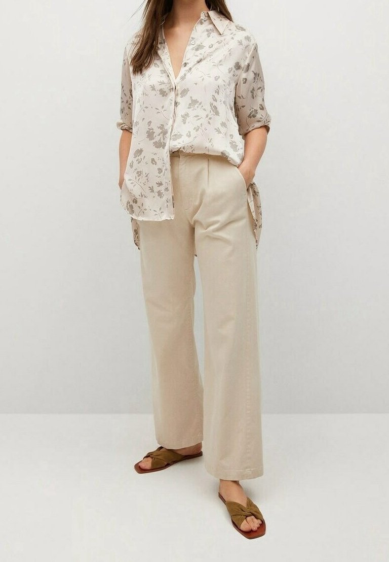 Lys beige bluse med blomsterprint, løstsiddende, med korte ærmer. Sammen med beige bukser med brede ben og olivengrønt slip-on sandaler.