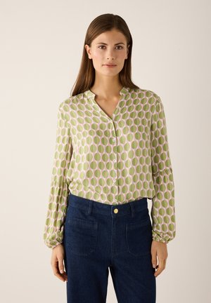 Groene blouse met roze cirkelpatroon, knoopsluiting aan de voorkant en geplooide mouwen. Gecombineerd met een donker denim broek met hoge taille.