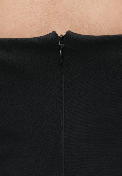 Melnas, ar rāvējslēdzēju aizdarāmas drēbes gabals ar teksturētu adījuma audumu. Rāvējslēdzējs atrodas centrā muguras pusē, tam ir melns slīdnis un lentiņa.