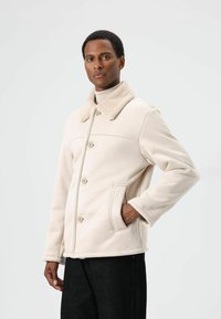 Crèmekleurig fleecejack met een zachte kraag, knopen aan de voorkant, zijzakken en een ontspannen pasvorm, gecombineerd met zwarte spijkerbroeken.