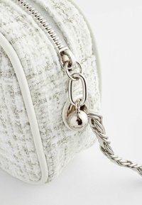Witte tweed tas met zilveren draadaccenten, voorzien van een metalen rits, ronde hardware en een gevlochten kettingband. Over het algemeen een gladde textuur.