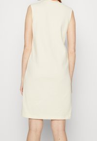 Bez rękawów, sukienka do kolan w kremowym kolorze, charakteryzująca się prostym fasonem i gładką teksturą. Brak widocznych wzorów lub detali sprzętowych.