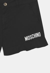 Černé šortky s volánkovým lemem, předními kapsami a bílým logem "MOSCHINO" vytištěným na levé noze. Zlatý detail knoflíku na pase.