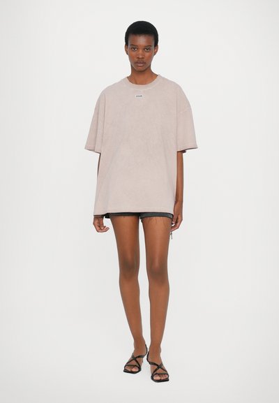 Oversized beige t-shirt with short sleeves, cotton blend fabric, features a small label at the neckline, paired with black distressed shorts.