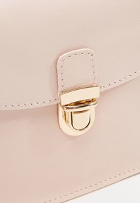 Primo piano di una morbida borsa in pelle rosa con una chiusura dorata e dettagli di cucitura, che mette in evidenza il suo design elegante e alla moda.