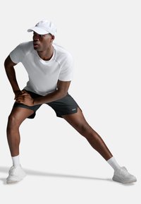 Sportowy strój składający się z dopasowanej białej koszulki i czarnych szortów. Biała czapka, białe skarpetki i białe tenisówki. Prosty design z materiałem odprowadzającym wilgoć.