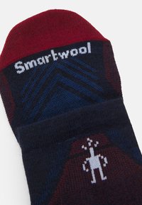 El calcetín Smartwool en azul marino y burdeos presenta patrones geométricos y un diseño de personaje en el pie, con un puño acanalado para un ajuste seguro.