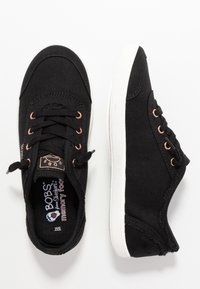 Black canvas sneakers with round toe, white rubber sole, copper eyelets, and a memory foam insole. Features a logo on the tongue.