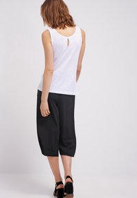 Vit ärmlös topp med ett nyckelhål bak, tillsammans med lösa svarta cropped byxor, vilket framhäver mjuka texturer och kontrasterande färger.