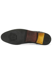 Suela de zapato de cuero negro con una superficie lisa, detalle de logo estampado, acento de cuero marrón y un talón reforzado con tachuelas metálicas.