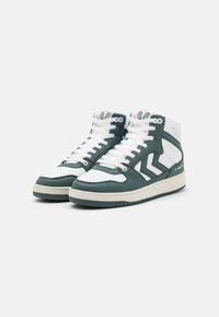 Para białych i ciemnozielonych wysokich sneakersów z białymi sznurówkami i wzorem w zygzak po bokach, na tle gładkiego białego tła.