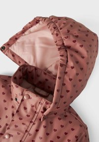 Rosa vattentät jacka med små burgundamönster av hjärtan, med fodrad huva och knappstängningar. Slät, glänsande yttextur.