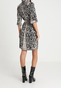 Abito camicia con una stampa di serpente in bianco e nero, maniche corte, vita cintrata e colletto. Abbinato a stivali neri lucidi con tacco.