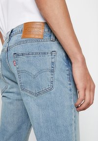 Ljust blå denimjeans med rak passform, med en läderlapp på midjan och en klassisk design på bakfickan.