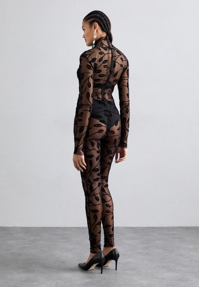 Sheer black bodysuit with leaf pattern, long sleeves, high neck, and fitted design. Paired with black high heels.