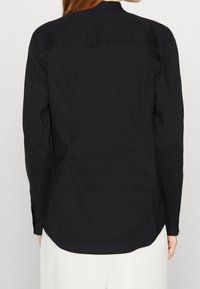 Camisa negra de manga larga con textura suave, dobladillo redondeado y detalle de pliegue en la parte posterior para mayor forma y comodidad.
