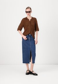 Brun strikket cardigan med knappelukking, parret med et langt denimskjørt med en frontslitt. Svarte sko fullfører antrekket.
