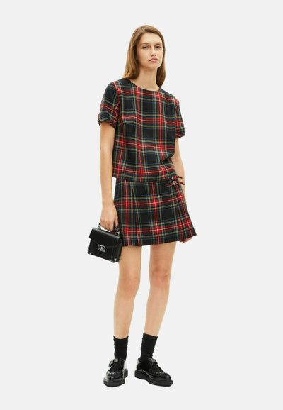 Donna che indossa un top a maniche corte a quadri rosso e nero e una gonna coordinata, con una borsa nera, calze nere e mocassini.