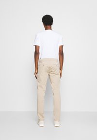 Pantalones chinos beige hechos de sarga de algodón, corte regular, pierna recta, con bolsillos traseros y detalles de costuras discretas, combinados con una camiseta blanca.
