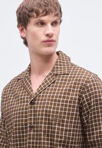 Braunes kariertes Hemd mit einem Reverskragen, ausgestattet mit einer Knopfleiste, einer akzentuierten Tasche und einer dezenten Logo-Stickerei auf der Brust.