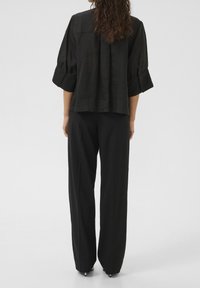 Haut en lin noir avec un dos plissé, manches trois-quarts et poignets boutonnés, associé à un pantalon large noir.