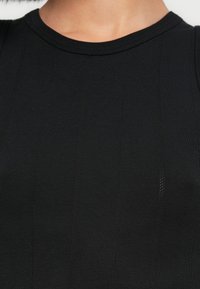 Débardeur noir côtelé avec encolure ronde et rayures verticales texturées. Le matériau semble extensible et ajusté.