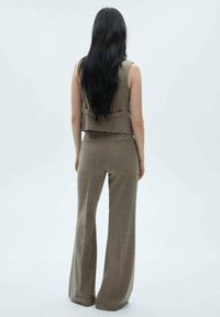 Brązowy zestaw składający się z kamizelki i szerokich spodni, uszyty z teksturowanej tkaniny, z tylną kieszenią w kamizelce, widoczny z tyłu na jasnym tle.