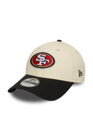 Beige színű baseball sapka fekete napellenzővel, elöl hímezett piros és fehér logóval, hátul pedig állítható pánttal.