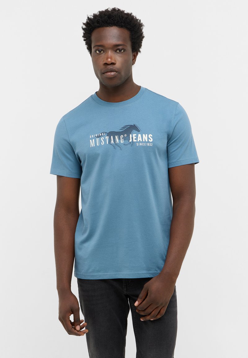 Niebieska bawełniana koszulka z krótkim rękawem i okrągłym dekoltem, z graficznym nadrukiem konia oraz napisem "MUSTANG® JEANS od 1932."