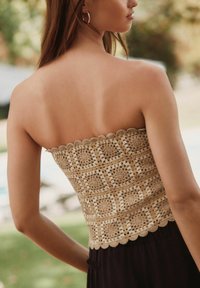 Top senza spalline realizzato in materiale crochet testurizzato di color beige chiaro, con orlo ondulato e motivi geometrici con trame aperte.