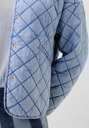 Veste synthétique matelassée en bleu clair avec un motif en losanges, dotée de boutons-pression dorés et d'une poche latérale. Finition en tissu texturé.