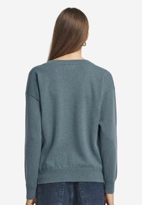 Ljusblå stickad tröja med avslappnad passform, sänkta axlar, ribbade muddar och fåll. Mjuk textur och minimalistisk design.