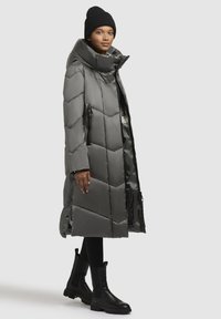 Puffarjacka i mörkgrått, med hög krage, geometrisk quiltning, dragkedjefickor på sidorna och accentuerad med svarta ankla stövlar.