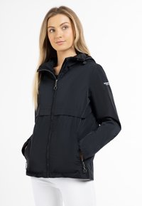 Giacca leggera nera con cappuccio, chiusura con zip e due tasche laterali. Il tessuto ha una consistenza liscia e presenta un design con patta frontale.