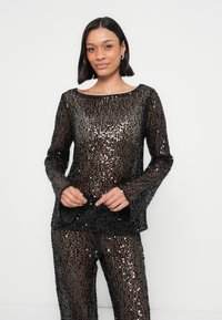 Haut noir et argenté à sequins avec manches longues, encolure ronde et poignets évasés, associé à un pantalon à sequins assorti.