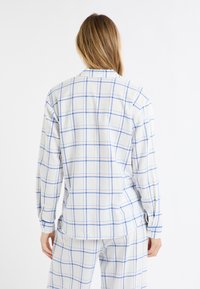Koszula flanelowa w kolorze białym z niebieskim wzorem w kratę. Posiada kołnierzyk, długie rękawy oraz rozcięcia po bokach na dole. Miękka w dotyku.