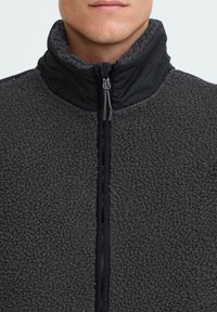 Fleece-Außenjacke in Dunkelgrau, mit hohem Kragen, durchgehendem Reißverschluss und einer weichen, strukturierten Oberfläche mit kontrastierenden schwarzen Akzenten.