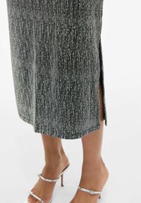 Robe midi noire avec des rayures métalliques argentées, dotée d'une fente sur le côté et d'une texture lisse. Portez-la avec des sandales à talons argentées.