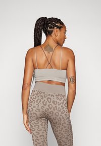 Lichtgrijze sportbeha met dunne bandjes, gecombineerd met high-waisted leggings met een beige luipaardprintpatroon. Gladde textuur, aansluitend ontwerp.